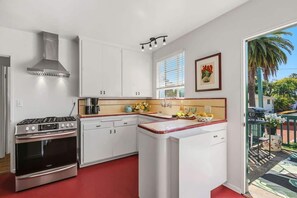 A kitchen with white cabinets, a stainless steel stove, and a window with blinds. - The Palm Terrace - West Beach Retreat (Santa Barbara)
