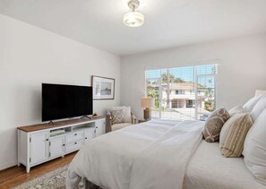 A bedroom with a bed, a TV, a bedside table, and a window with a view. - The Palm Terrace - West Beach Retreat (Santa Barbara)