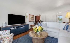 A living room with a flat-screen TV, a sofa, a coffee table with flowers, and a cabinet. - The Palm Terrace - West Beach Retreat (Santa Barbara)