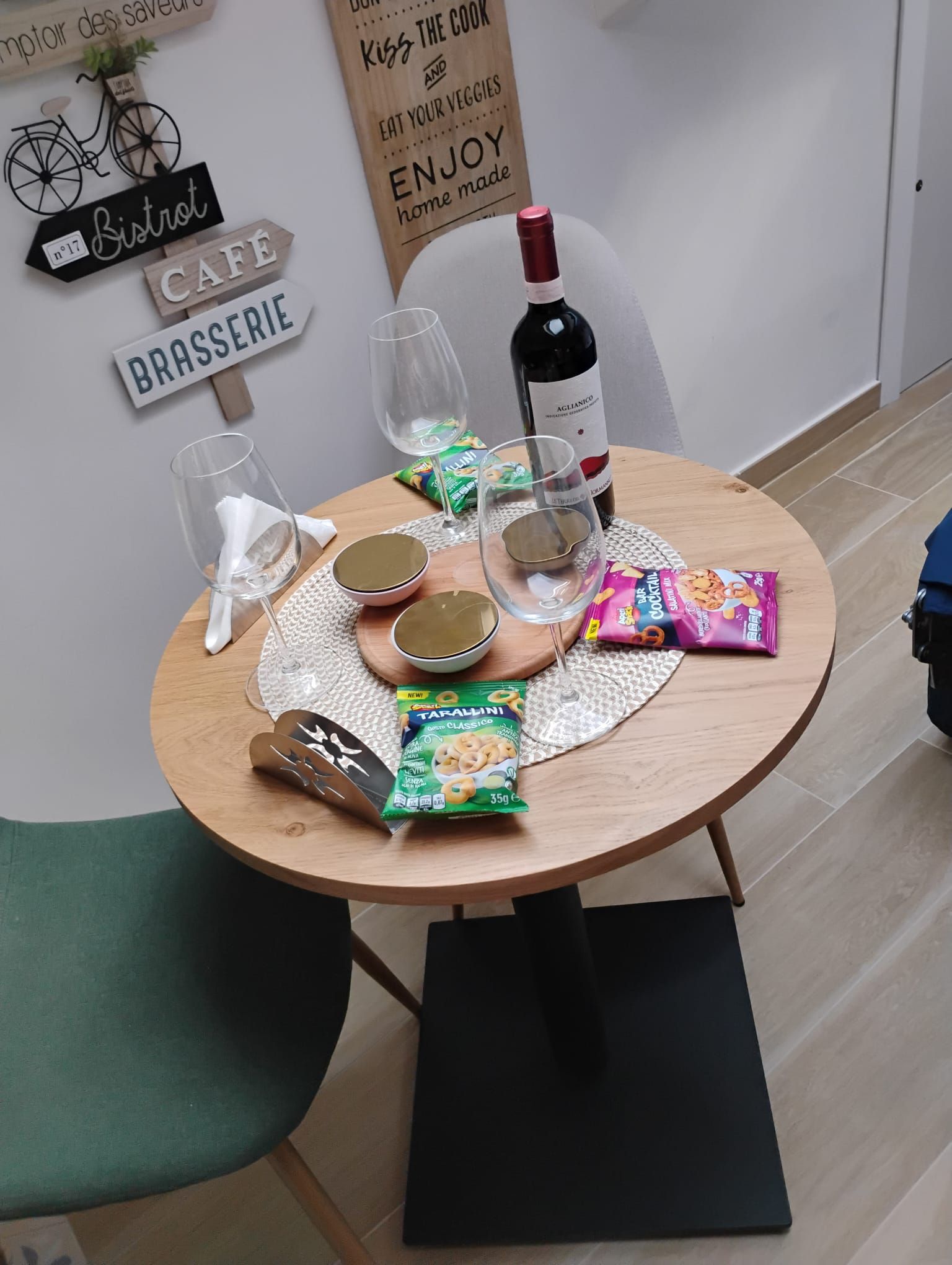 Mesa de madeira redonda com apoio para prato, copo de vinho, tigela e lanches embalados.
