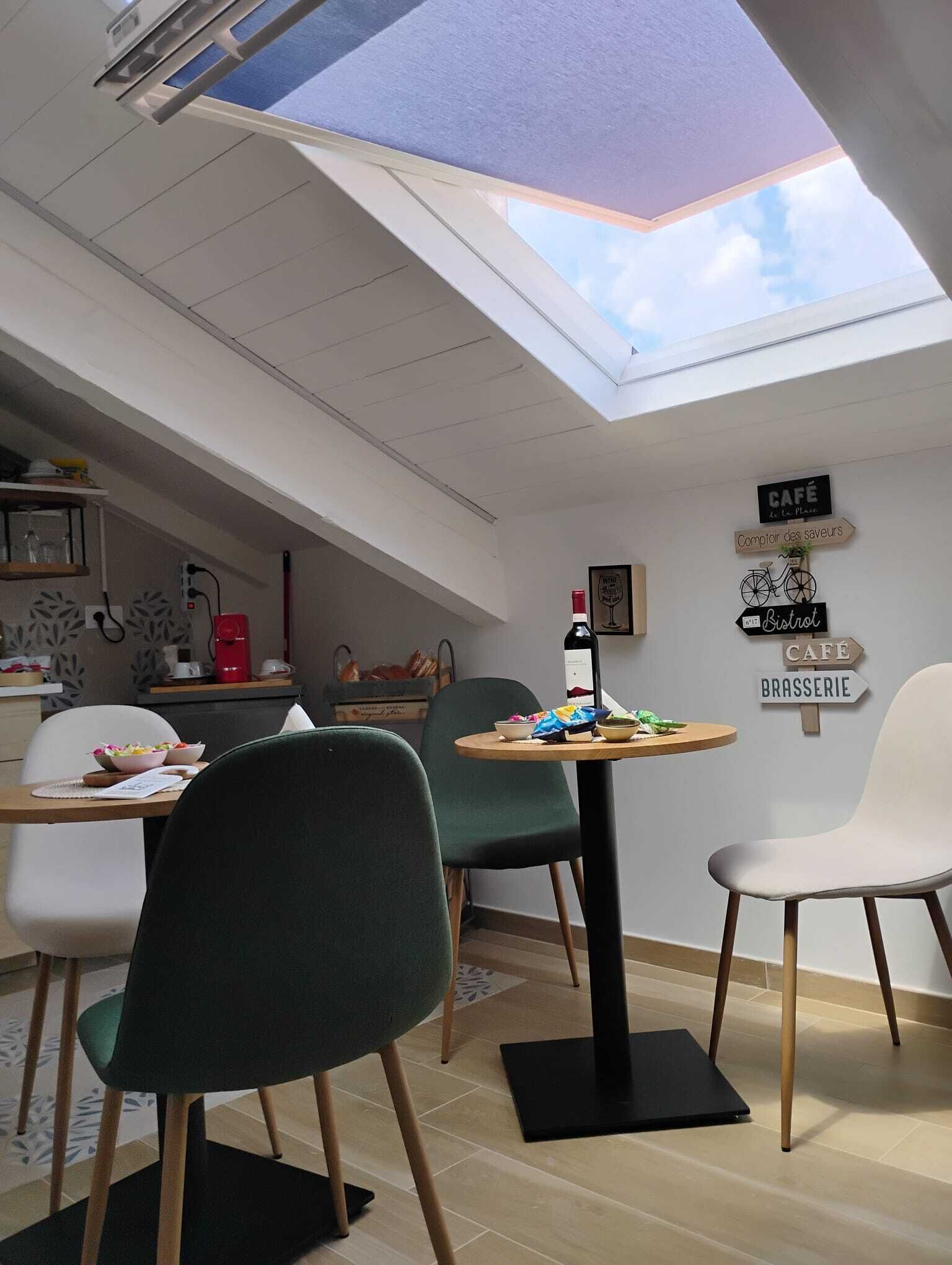 Una cocina moderna con tragaluz, una zona de comedor con sillas y mesa, y carteles en la pared que indican un café y una brasserie.