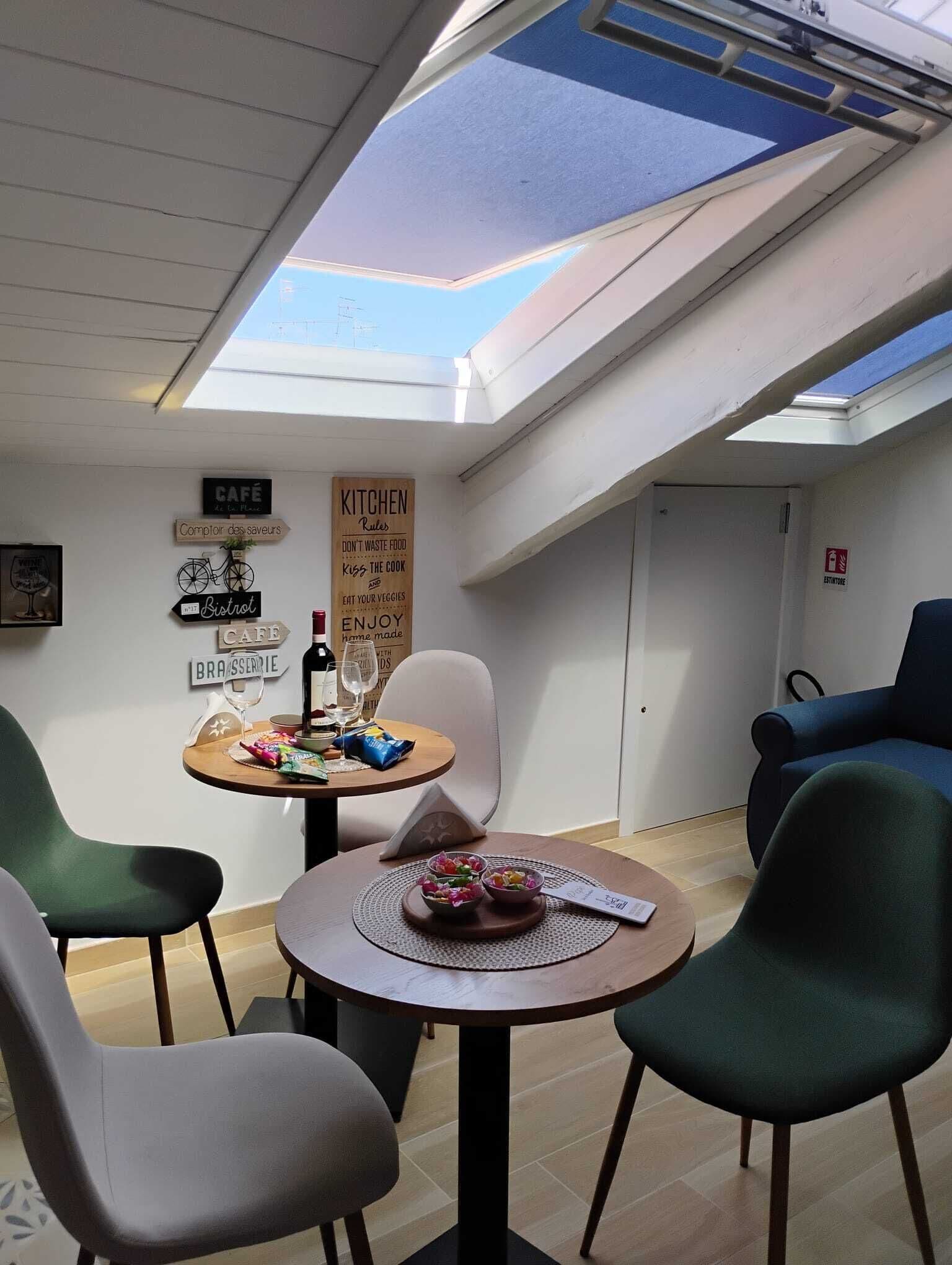 A dining area with a skylight, a table with a placemat, chairs, and wall signs including 'CAFE' and 'KITCHEN Rules'.