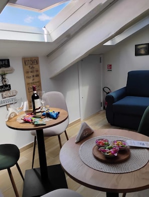 A small, cozy room with a skylight, a dining table with snacks and a bottle, a blue sofa, and a kitchen sign. - Pepè attic room Naples Central  (Naples)