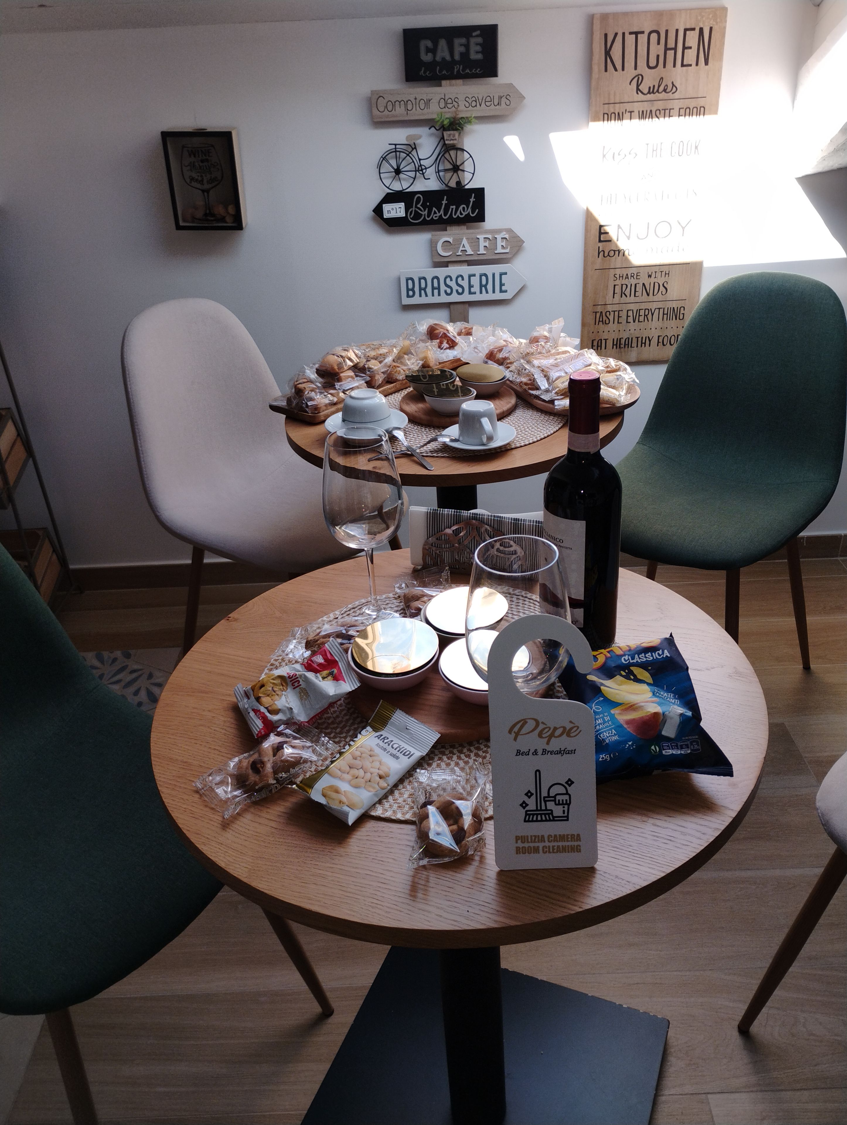 A dining table set with bread, pastries, and a bottle of wine, surrounded by chairs.