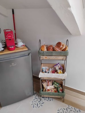 Une petite cuisine équipée d’une machine à café rouge, d’un petit réfrigérateur et d’un présentoir à pain contenant des viennoiseries.