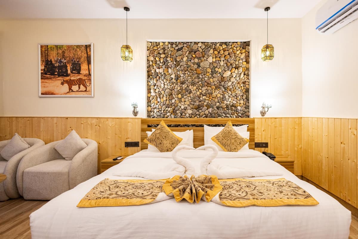 A hotel room with a wooden headboard, a bed with white linens and decorative pillows, a wall-mounted artwork, and a stone wall feature.