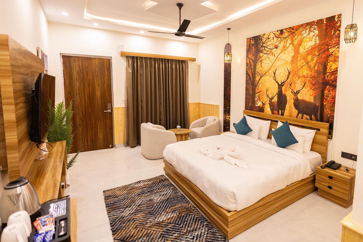 A modern hotel room with a large bed, a flat-screen TV, a desk with a coffee machine, and a painting of deer in a forest.
