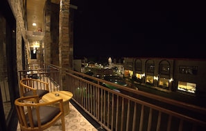 Un balcón con sillas de madera y una pequeña mesa, con vista a un complejo de edificios iluminado por la noche.