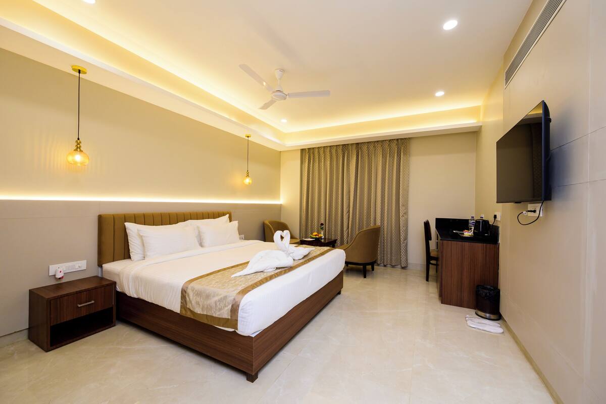 Una habitación de hotel con cama, escritorio, silla, televisor y ventilador de techo.