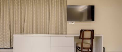A room with a white cabinet, a TV mounted on the wall, a wooden chair, and a curtain.
