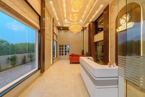A reception area with a reception desk, a red sofa, and a large window with a view of greenery. - Amritara The Samagam (Kaithi)