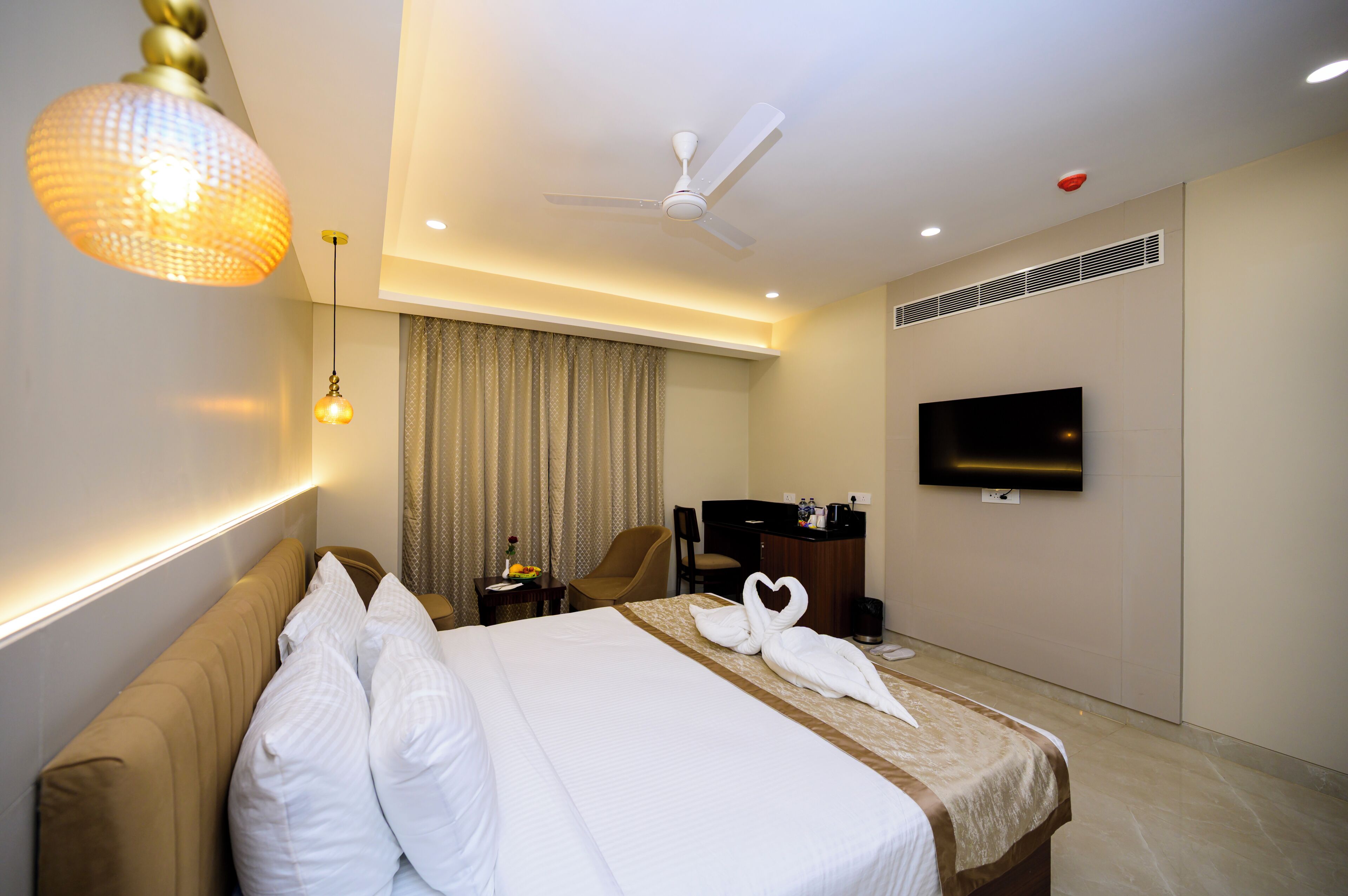 Ein Hotelzimmer mit Bett, Schreibtisch, Stuhl, Fernseher und Deckenventilator.