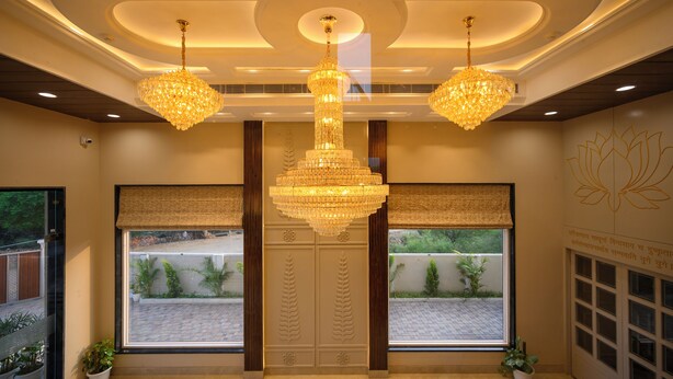 A lobby with a large chandelier, two windows with blinds, and a wall with a lotus design. - Amritara The Samagam (Pindra)