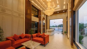 A modern hotel lobby with a reception desk, seating area with sofas, and a large window offering a view. - Amritara The Samagam (Pindra)