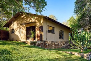 A single-story house with a stone foundation, a sloped roof, and a front porch with a potted plant. - Parsons River Camp (Hoedspruit)