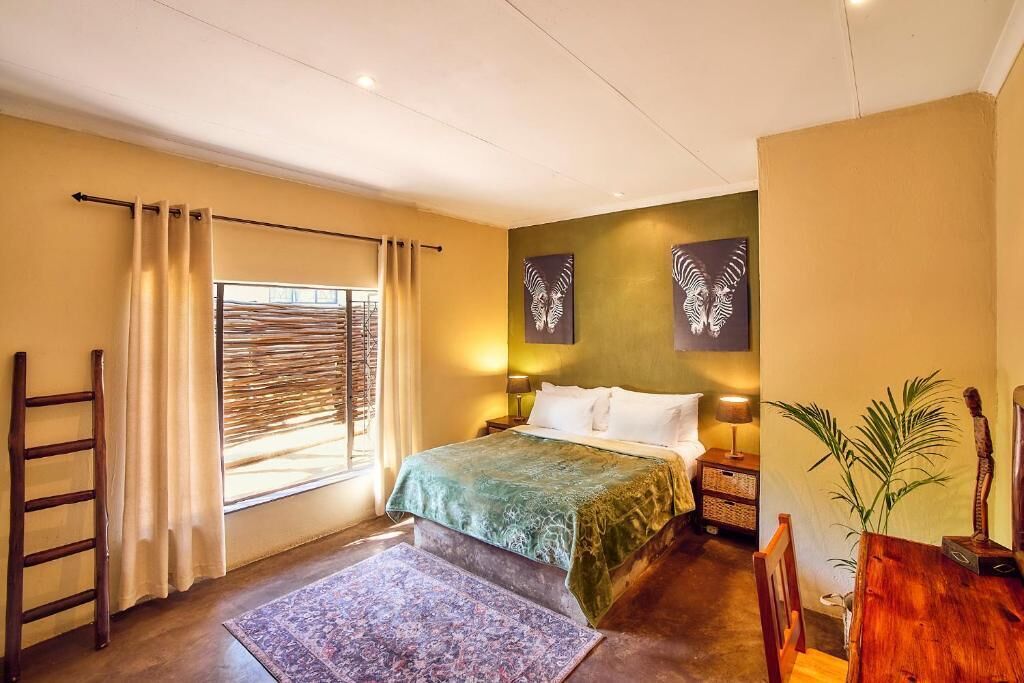 A bedroom with a bed, curtains, a ladder, a nightstand, a lamp, a wall-mounted artwork, and a plant.
