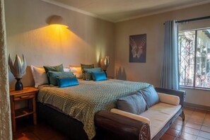 A bedroom with a bed, a sofa, a nightstand, and a wall-mounted lamp. - Parsons River Camp (Hoedspruit)