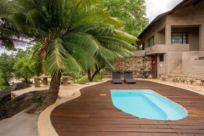 A pool area with a wooden deck, lounge chairs, and a palm tree. - Parsons River Camp (Hoedspruit)