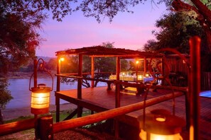 A wooden deck with a glass enclosure, a table set for dining, and a lantern. - Parsons River Camp (Hoedspruit)