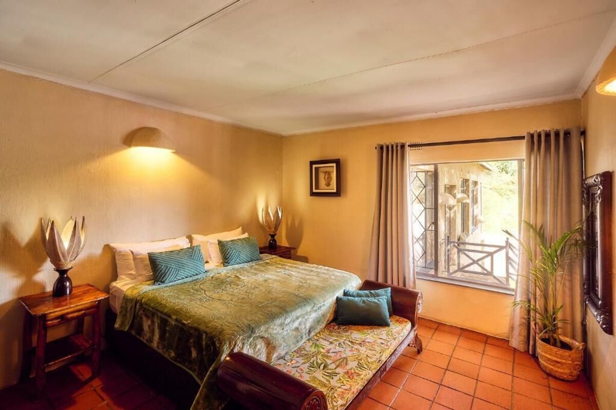 A bedroom with a bed, bedside tables, a window with curtains, and a view of the outside.