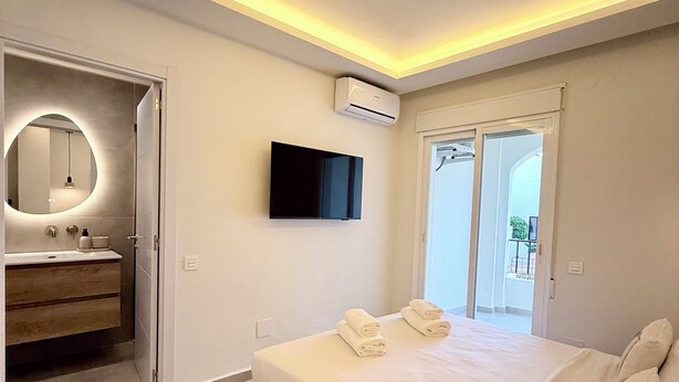 Quarto moderno com cama, televisão, ar condicionado e banheiro com espelho e pia.