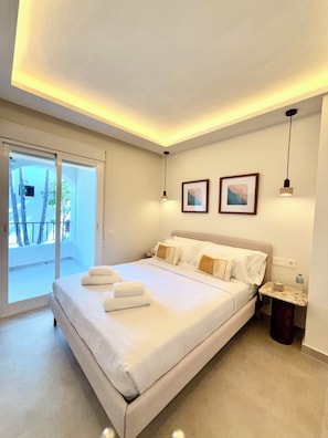Ein Hotelzimmer mit Bett, Nachttisch, Bilderrahmen, Deckenleuchte und Blick ins Freie.
