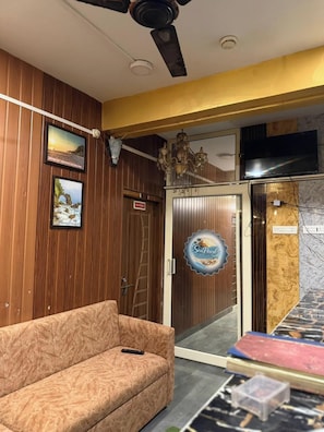 Recepció d'hotel amb paret de fusta, un sofà, un penjallum, un televisor i una porta amb un cartell.
