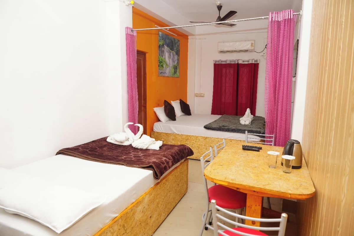 A small, compact room with two beds, a table with chairs, a ceiling fan, and a painting on the wall.