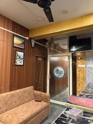 A hotel lobby with a wooden wall, a sofa, a chandelier, a TV, and a door with a sign. - Sea Pearl Homestay Andaman (Sri Vijaya Puram)