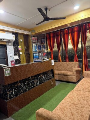 A reception area with a brick counter, a ceiling fan, a sofa, and a window with curtains. - Sea Pearl Homestay Andaman (Port Blair)