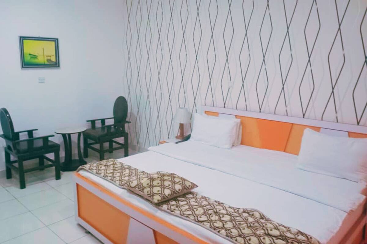 Habitación de hotel con cama, una mesita, dos sillas, una lámpara de pared y un cuadro.