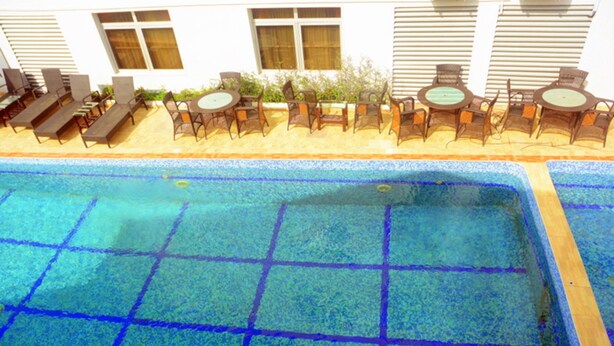Una piscina con bordes azulejados, sillas de descanso y mesas dispuestas a su alrededor.