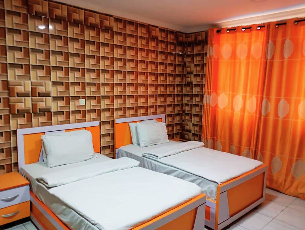 A room with two beds, a patterned wall, and orange curtains.