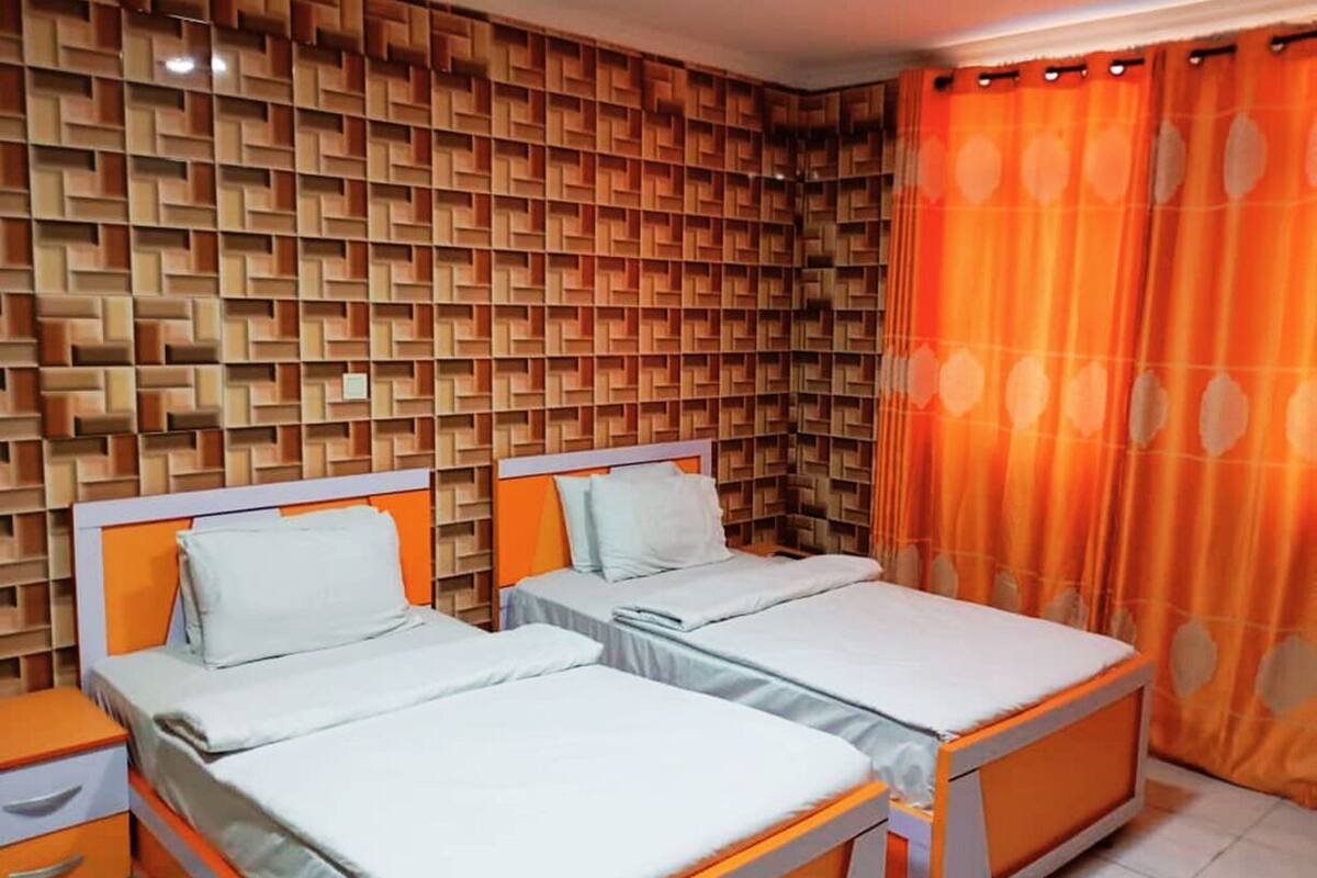 Una habitación con dos camas, un papel tapiz estampado y cortinas naranjas.