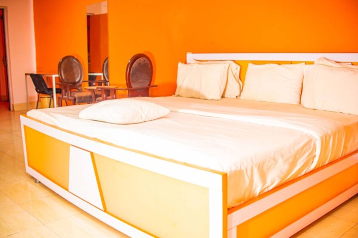 Una cama con cabecera y piecera blancos, una mesita de noche y una silla en una habitación con paredes naranjas.