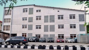 Un edificio de varios pisos con fachada de tejas, varias ventanas con contraventanas y un estacionamiento con distintos automóviles.