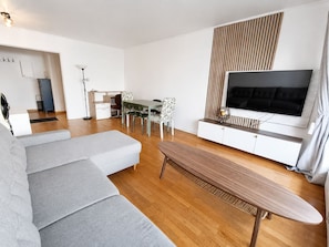 A modern living room with a sofa, dining table, chairs, a TV, and a wooden floor. - Serenity Courbevoie, Paris La Défense (Courbevoie)