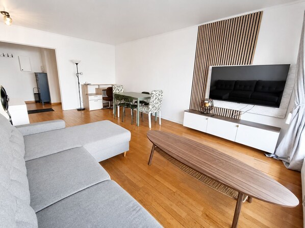 Uma sala de estar moderna com sofá, mesa de jantar, cadeiras, televisão e piso de madeira.