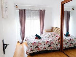 Une chambre à coucher avec un lit en bois, une literie à motifs floraux, un miroir et un plancher en bois.