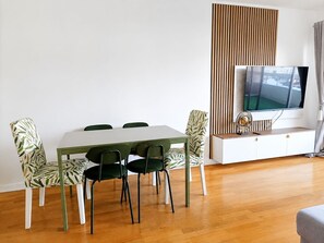 Uma área de refeições com mesa, cadeiras, televisão e piso de madeira.