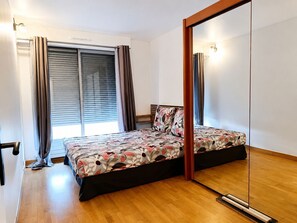 A bedroom with a bed, a mirror, a window with curtains, and a wooden floor. - Serenity Courbevoie, Paris La Défense (Courbevoie)