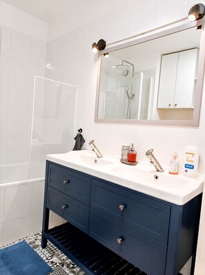 A bathroom with a white sink, dark blue vanity, a large mirror, and a shower. - Serenity Courbevoie, Paris La Défense (Courbevoie)