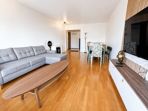 Un salon moderne avec un canapé gris, une table basse en bois et un coin repas agrémenté d’une nappe à motifs.
