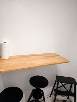 A wooden shelf with a roll of toilet paper, a black stool, and a black chair. - Serenity Courbevoie, Paris La Défense (Courbevoie)