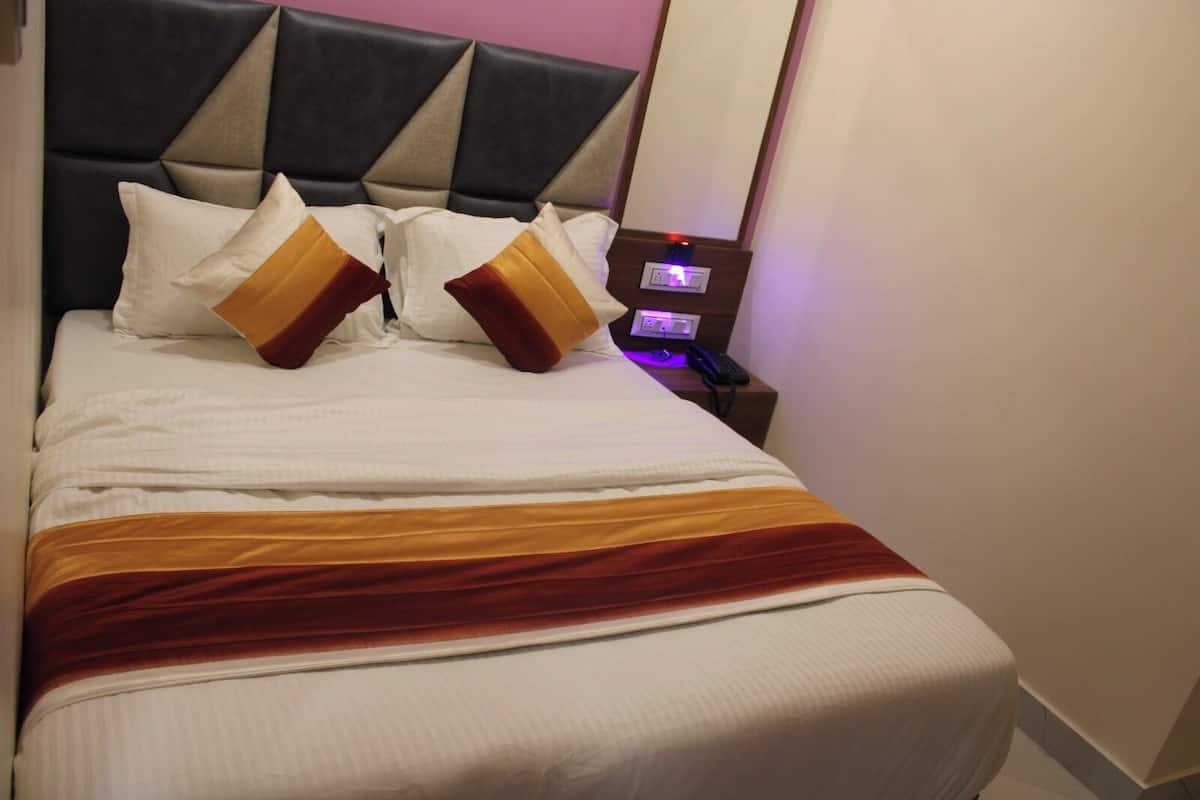 A neatly made bed with a headboard, pillows, and a bedside table with a phone and a power outlet.