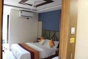 A hotel room with a bed, a ceiling fan, an air conditioning unit, a mirror, and a door with a number sign.