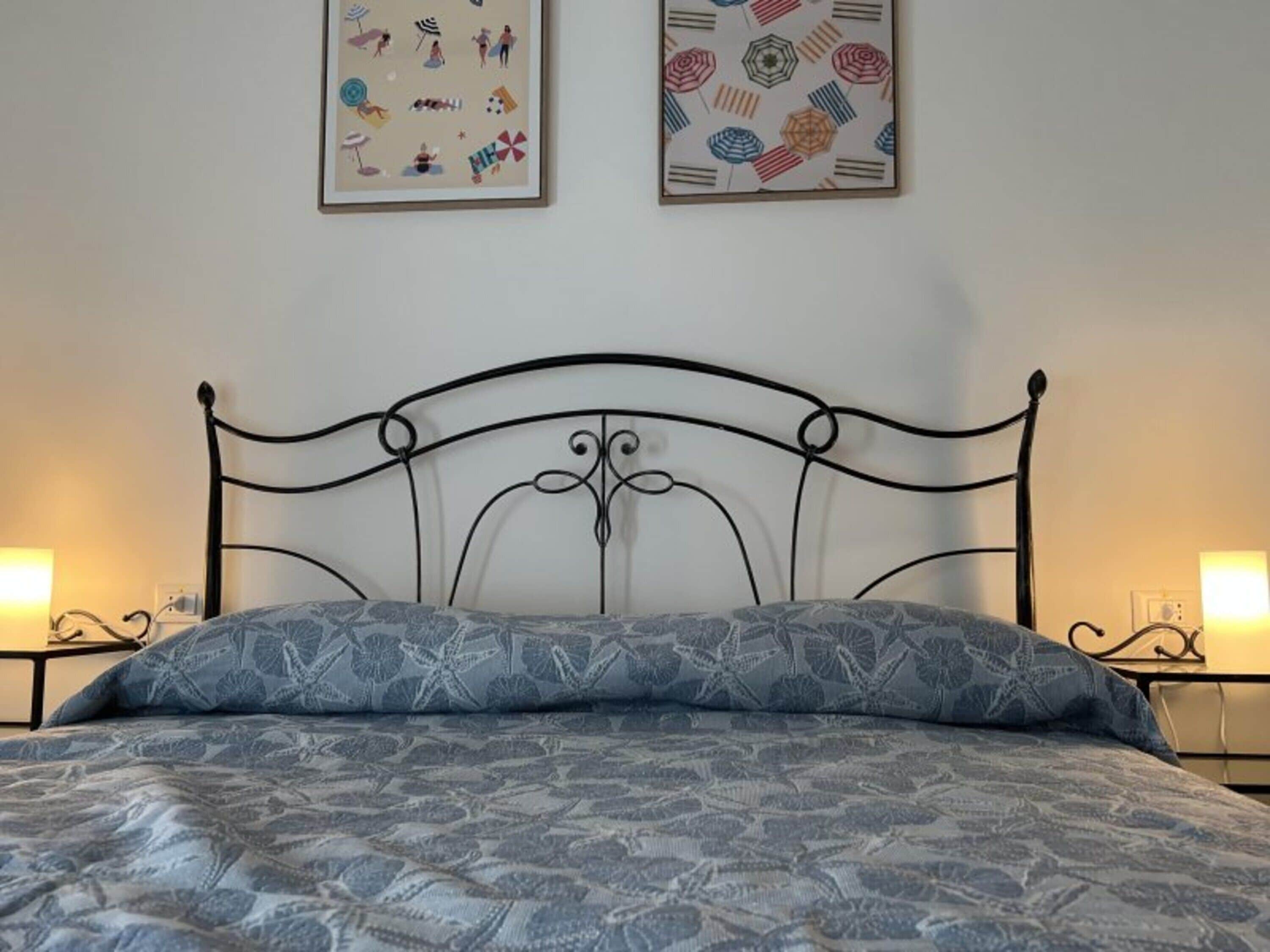 A bed with a metal headboard, a patterned bedspread, and two wall-mounted lamps.