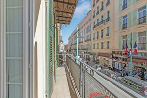 Ein Balkon mit Blick auf eine belebte Straße, an der sich Gebäude und ein Fußweg befinden, mit einem Schild für 'Agence Inter Immobilier'.