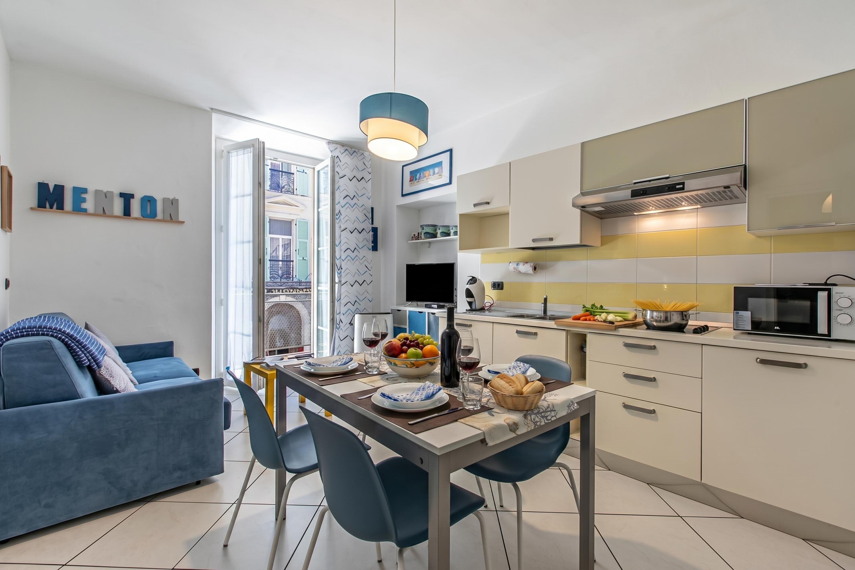 Un salon moderne avec un canapé, une table à manger et des chaises. On aperçoit également un coin cuisine équipé de placards et d’appareils électroménagers.
