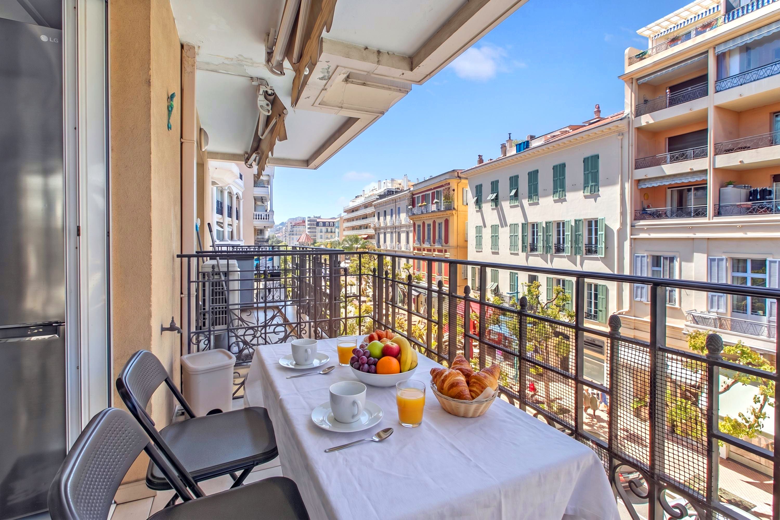 A balcony with a table set for breakfast, including croissants, fruit, and juice.